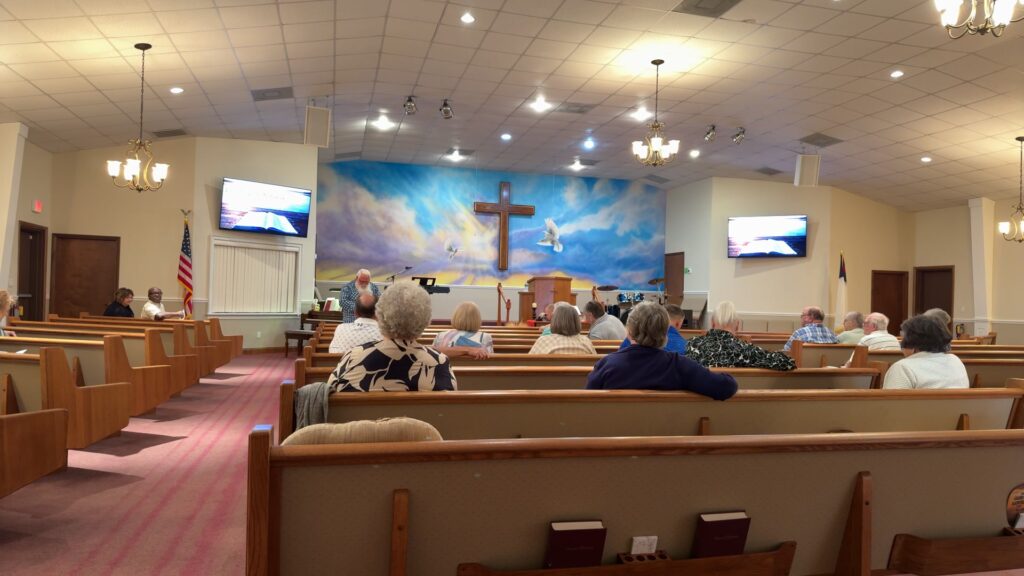 Congregation gathered for worship at Sugarloaf Church with cross mural backdrop